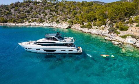 White yacht with sun deck and platform, turquoise sea and rocky shoreline in background