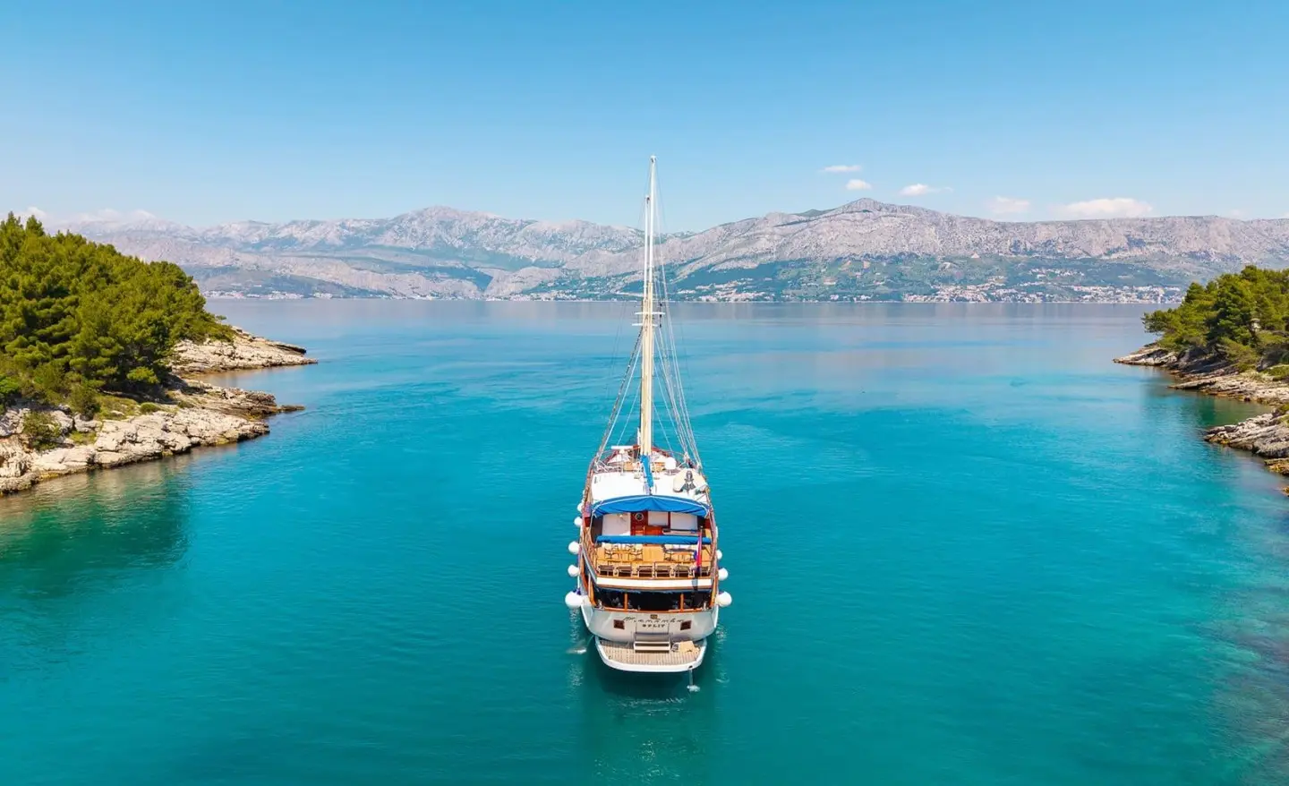Gulet Mendula anchored in clear turquoise water with hills in the background