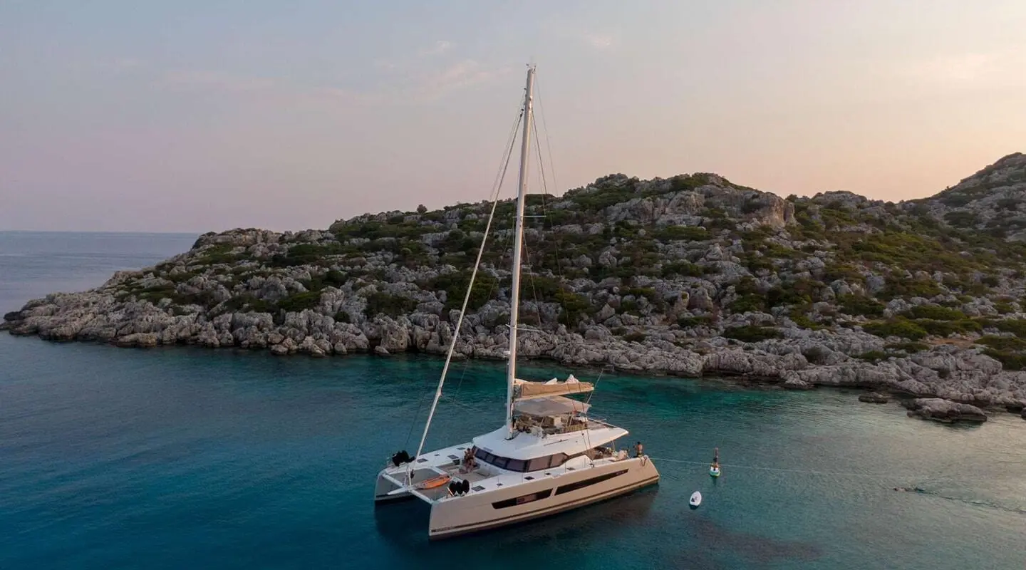 Serenissima luxury yacht anchored near rocky coastline at sunset