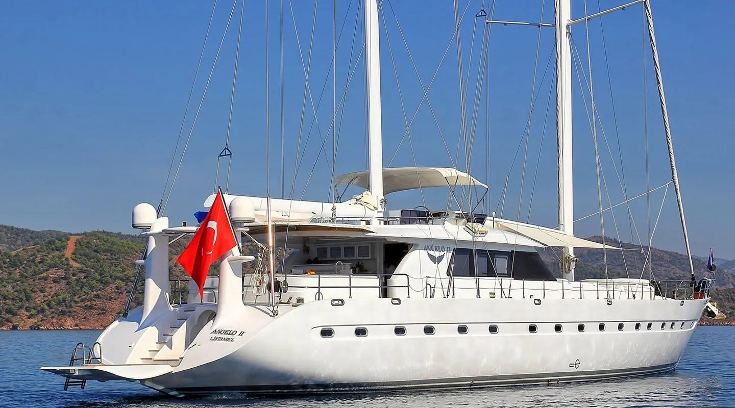 Angelo II gulet anchored, rear view shows sails, deck, and red flag