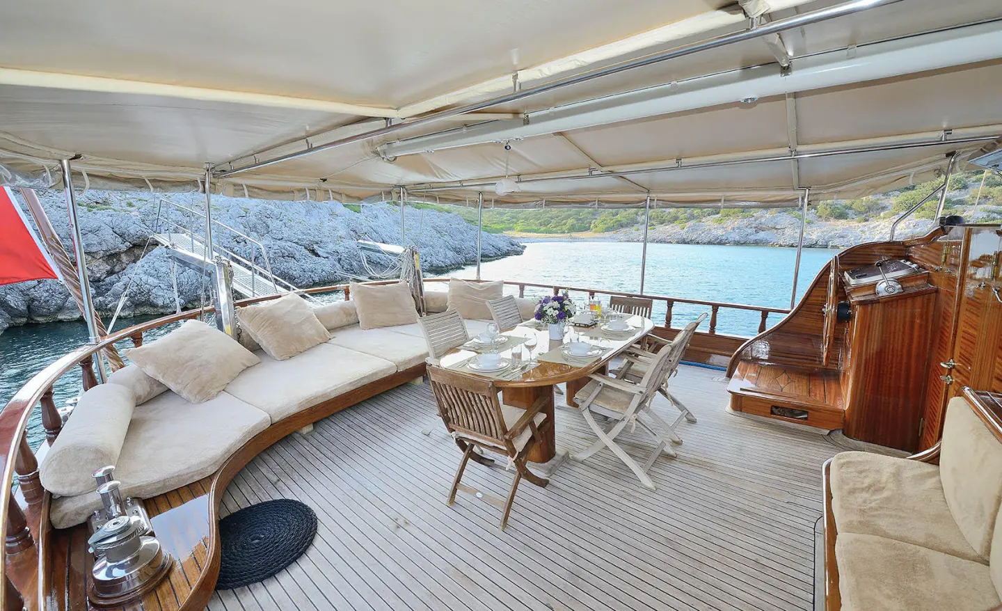 Open deck with cushioned seating and a dining table overlooking sea and rocky coastline