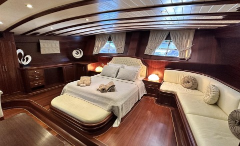Wood-paneled yacht cabin with a large bed, bedside lamps, and a curved sofa area near windows