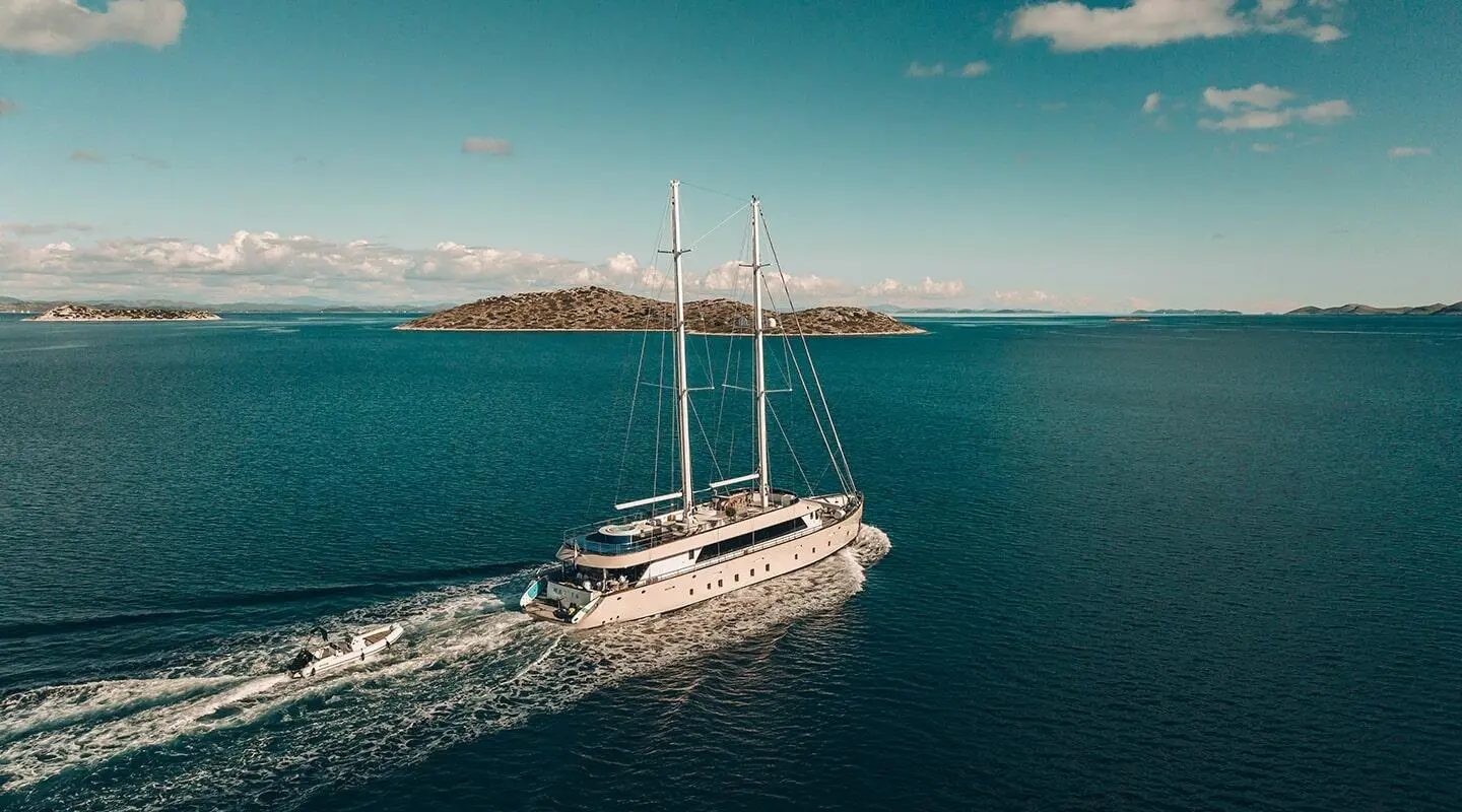 A luxury sailing yacht Maxita glides through turquoise harbor waters under clear sky