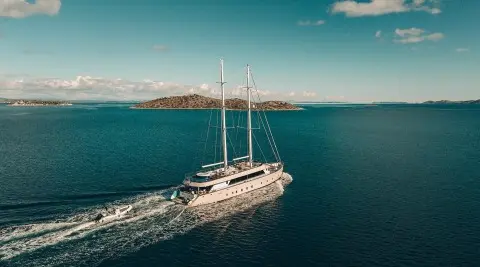 A luxury sailing yacht Maxita glides through turquoise harbor waters under clear sky
