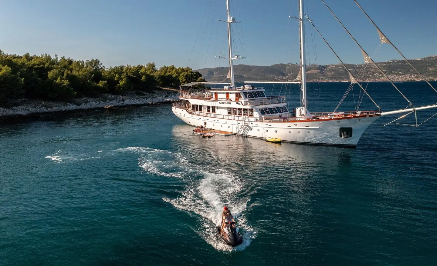 Corsario yacht anchored near rocky shoreline at sunset with calm blue sea