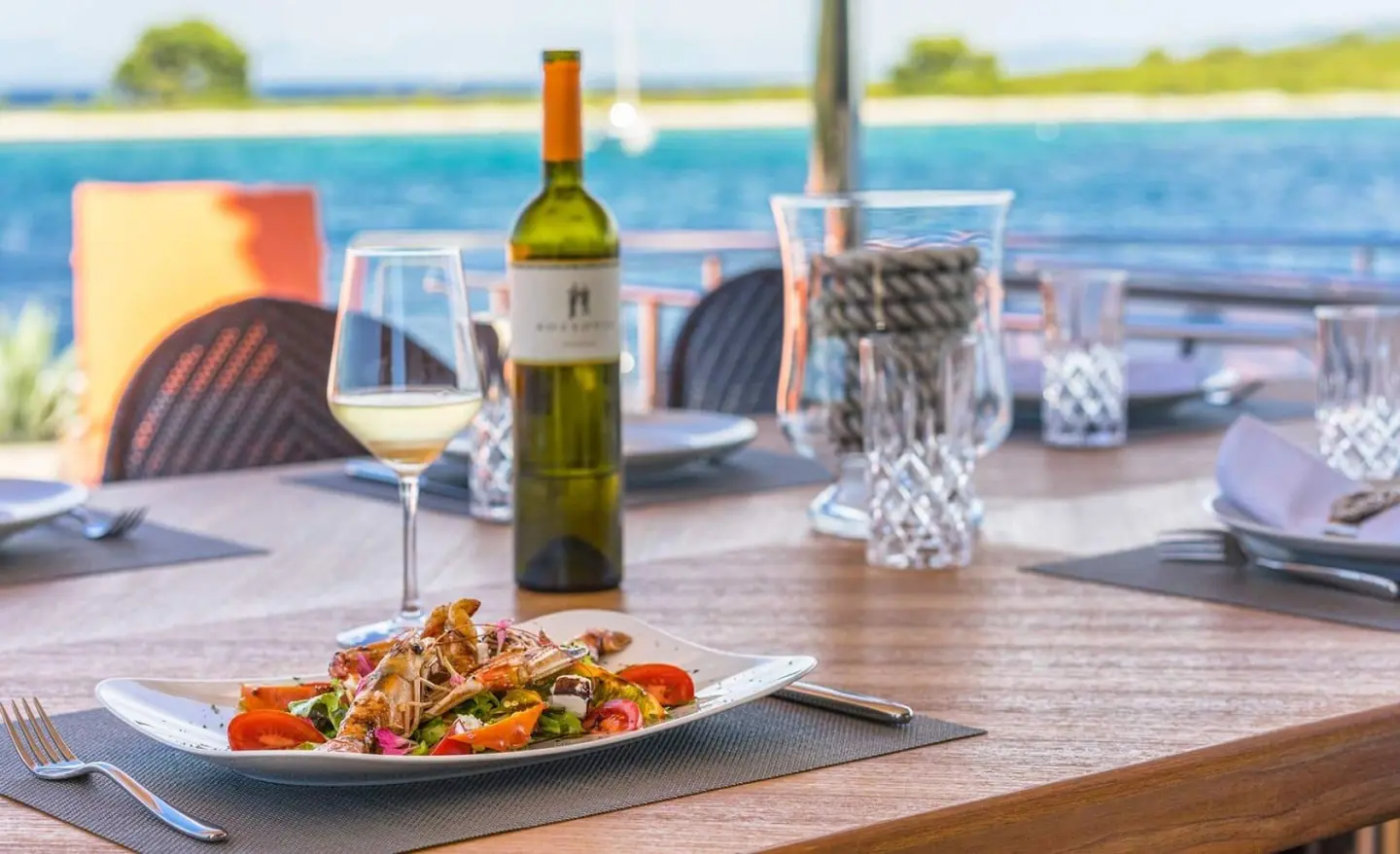 Seventh Sense yacht deck dining scene with wine, plate of food, and ocean view