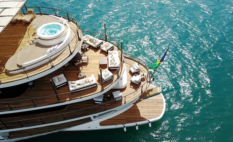 Aerial view of a luxury yacht deck with seating areas and a hot tub, wooden decking, turquoise sea