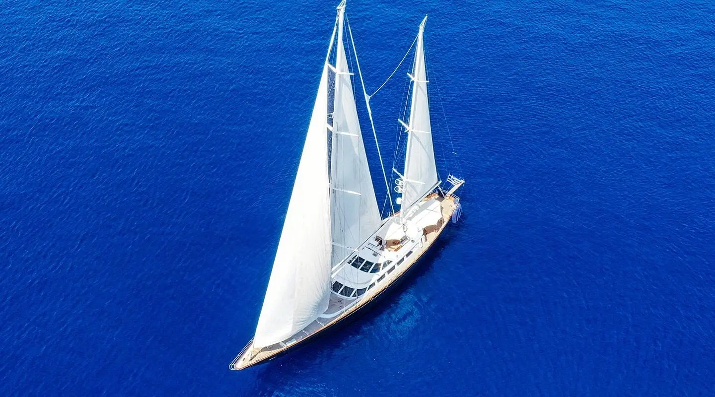 Sailing yacht Tamarita with white sails on deep blue sea, aerial view