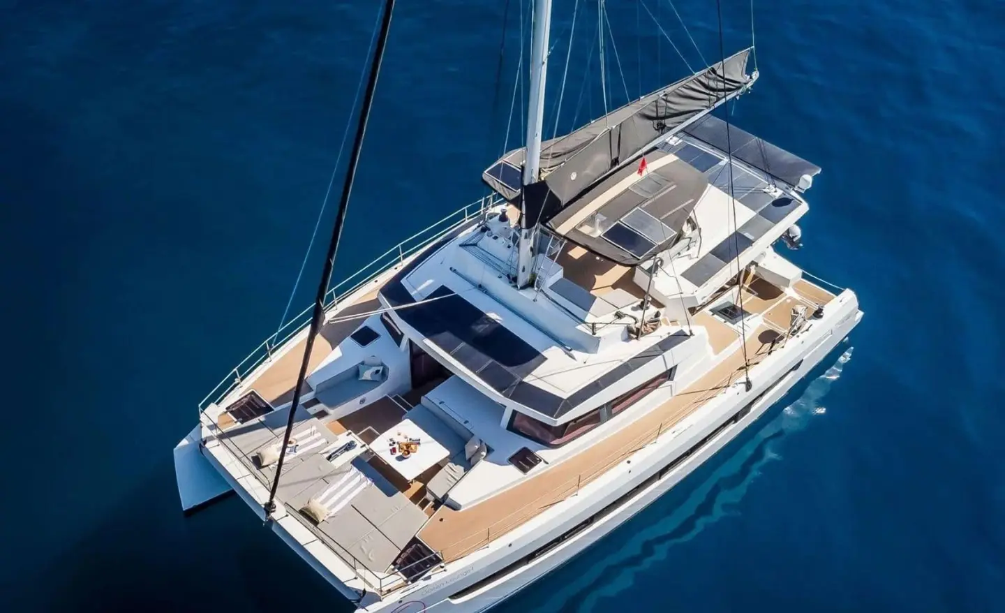Top-down view of a luxury catamaran yacht anchored in blue water with deck seating