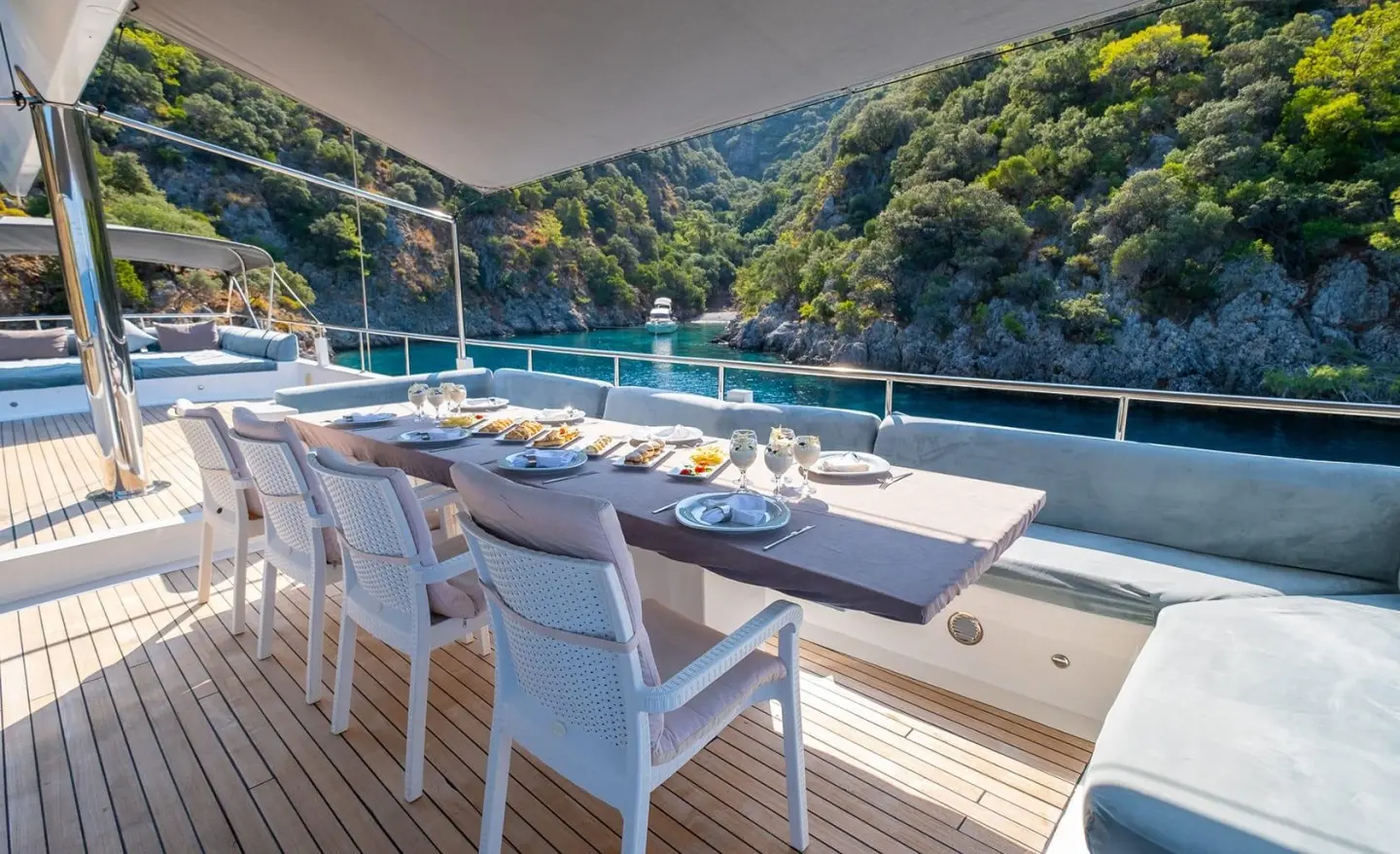 Esma Sultan yacht deck with white seating, dining table, and scenic hillside backdrop