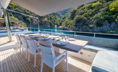 Esma Sultan yacht deck with white seating, dining table, and scenic hillside backdrop