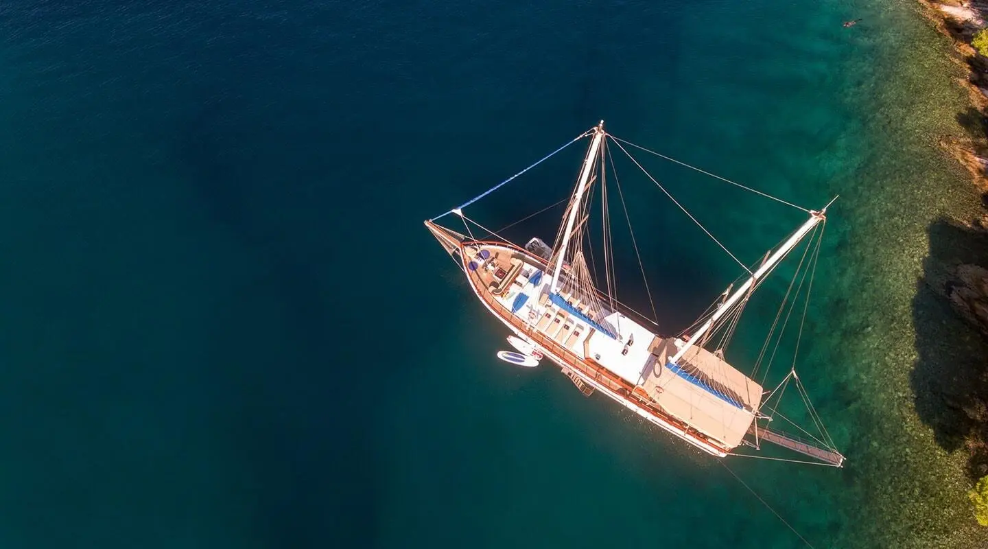 Aerial view of a small luxury sailing yacht named Malena anchored on calm blue-green water at sunset