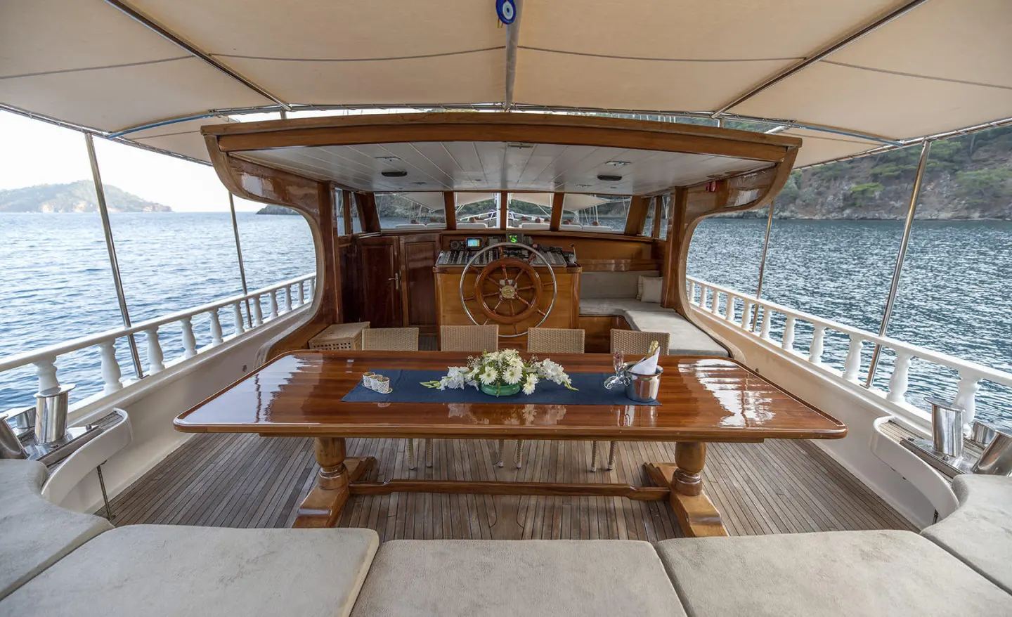 Kayhan 8 yacht deck with wooden helm, seating, and steering wheel at sunset