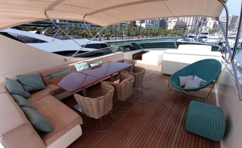 Miraval yacht deck with cream seating, teal cushions, wicker chairs, and a teak table on a sunny marina backdrop