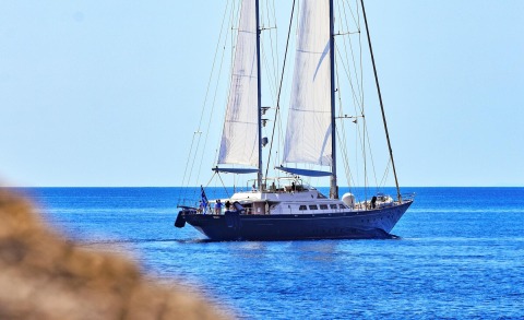 A luxury sailing yacht Tamarita seen from the deck with white sails and blue hull on the open sea horizon