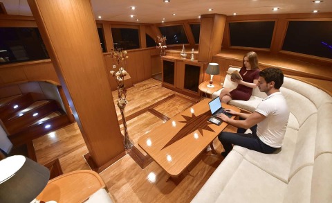 Interior yacht saloon with wooden decor and a central table with two people seated