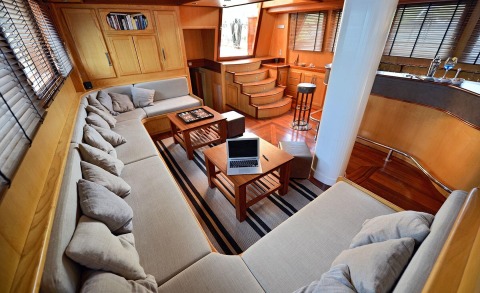 Interior of the yacht with a corner sofa, wooden coffee table, and an open laptop on a table