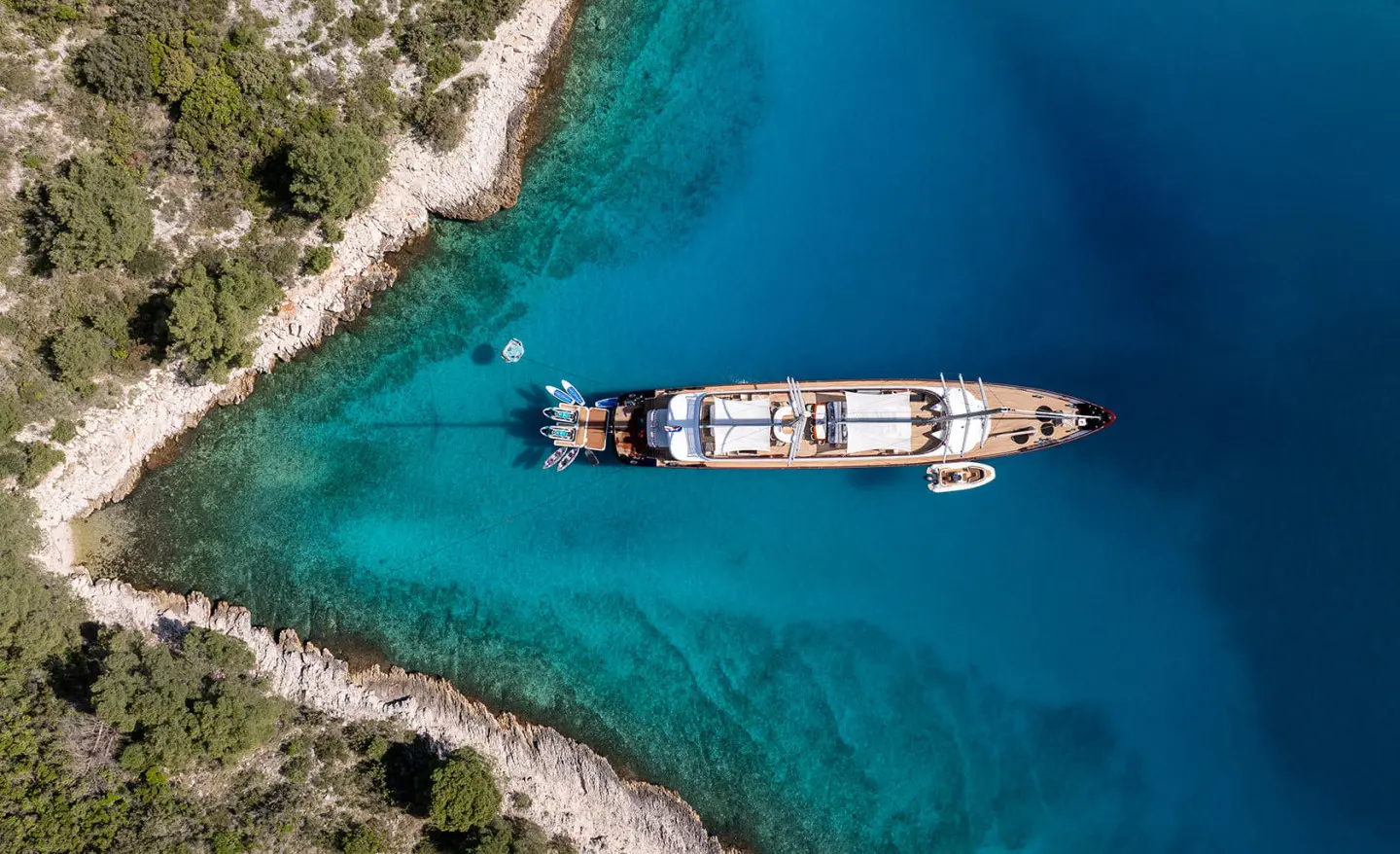 Nocturno luxury yacht anchored in crystal blue water near rocky shoreline at sunset