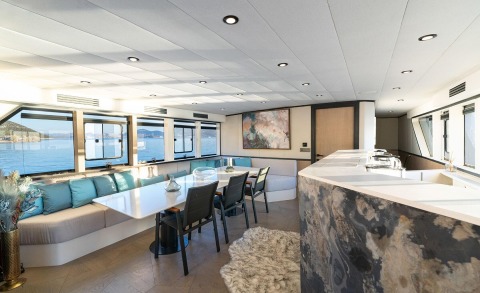 Interior of a motor yacht with a long dining table, seating area and large windows overlooking the sea, modern decor and lighting