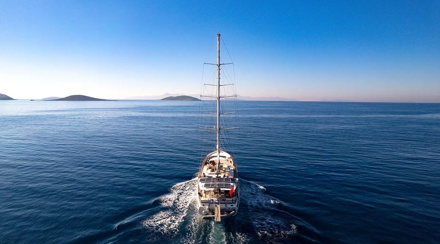 Tall sailing yacht seen from behind on open sea with single mast and wake