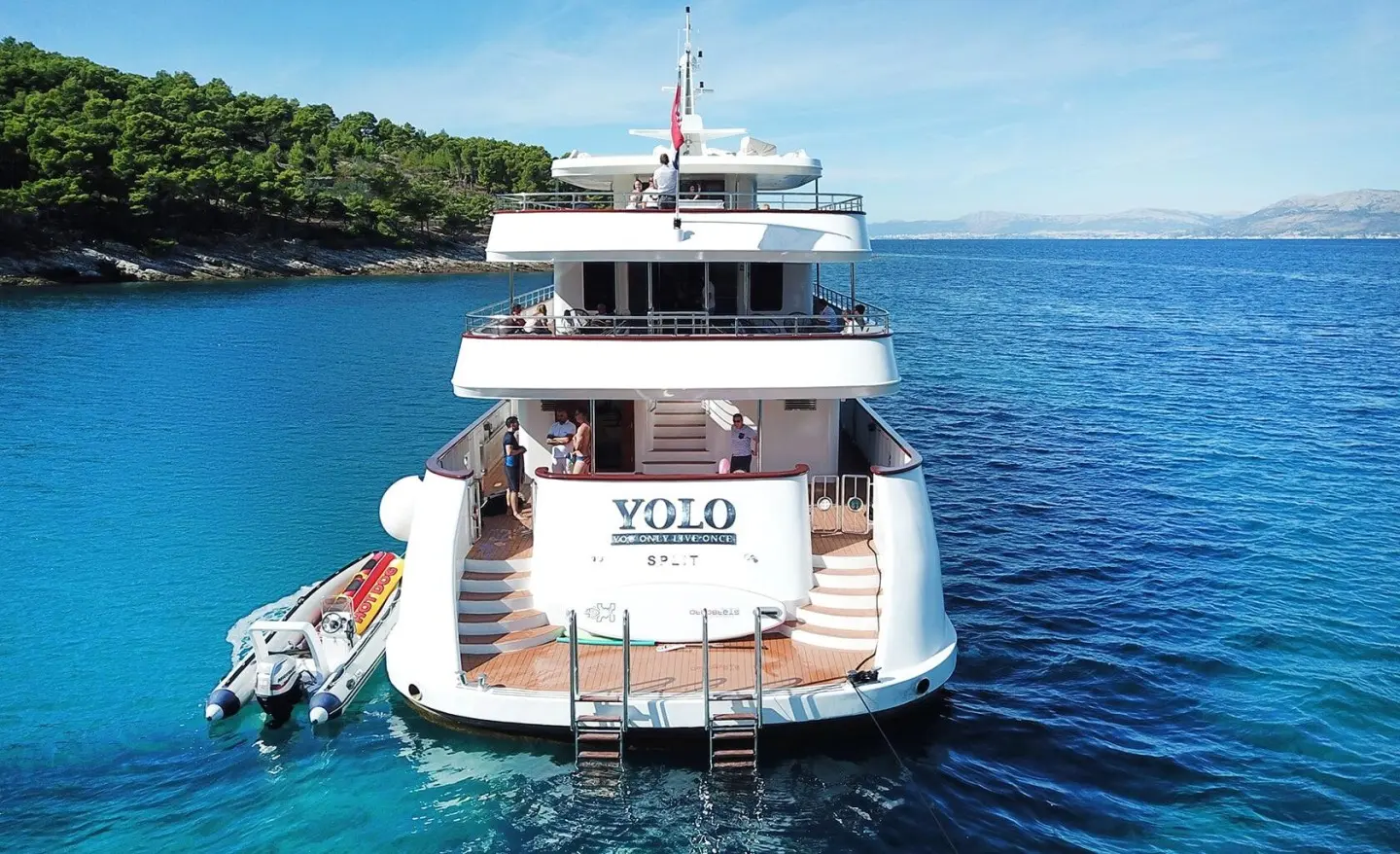 Yacht named Yolo seen from stern, docked on calm blue sea