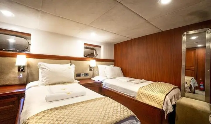 Twin cabin aboard Virtuoso yacht with two single beds and warm wood paneling
