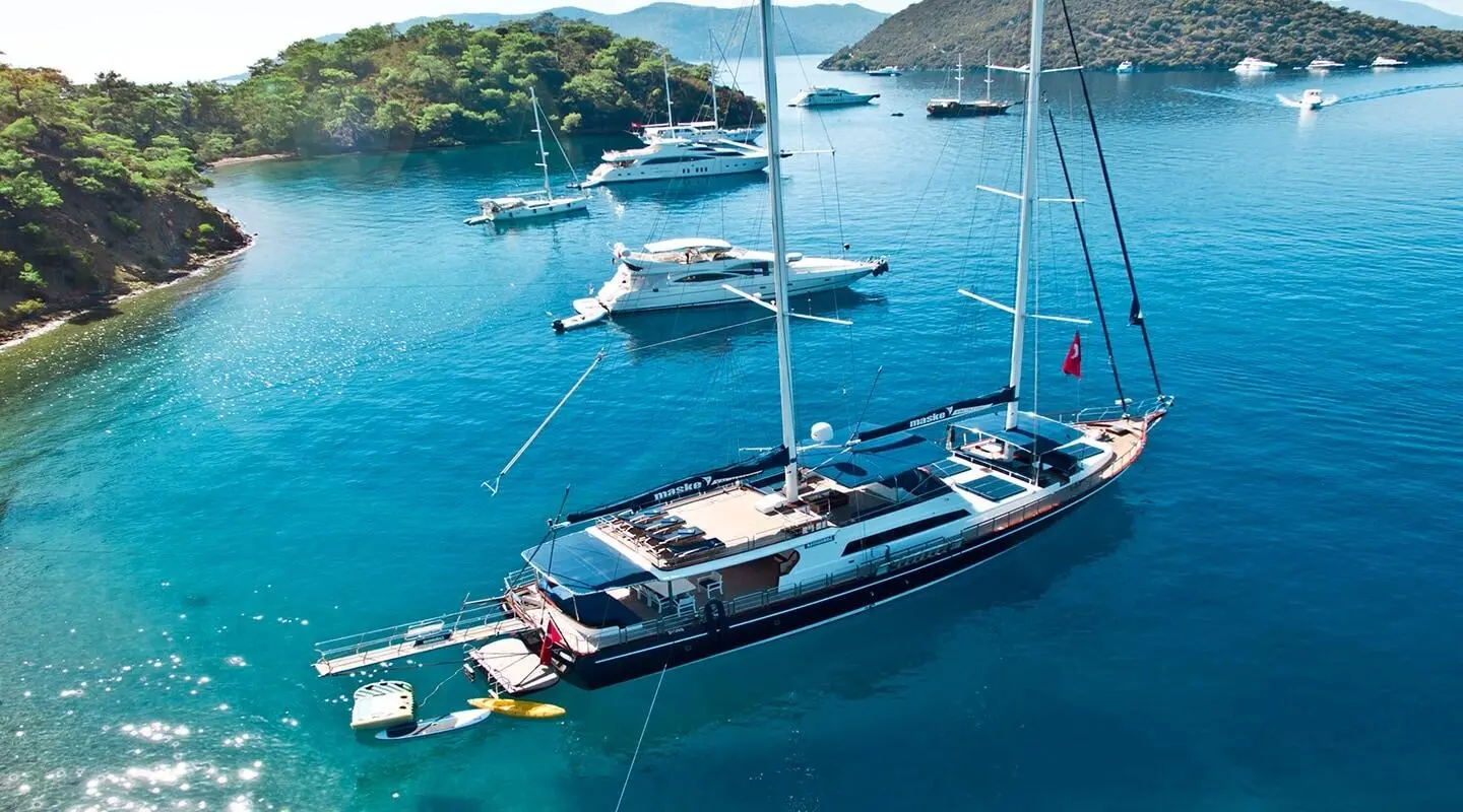 Maske 2 yacht anchored beside rocky coast near turquoise waters at sunset