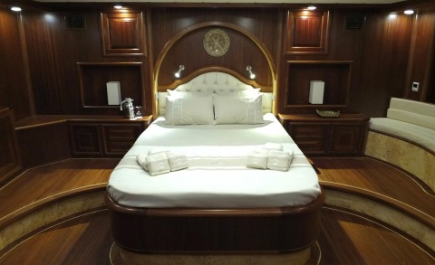 Lux wooden-paneled yacht cabin with a centered bed, tufted headboard, built-in cabinets, and soft lighting