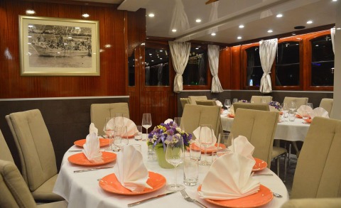 Interior of a yacht dining room with wood panel walls, white tablecloths, orange plates and arranged place settings