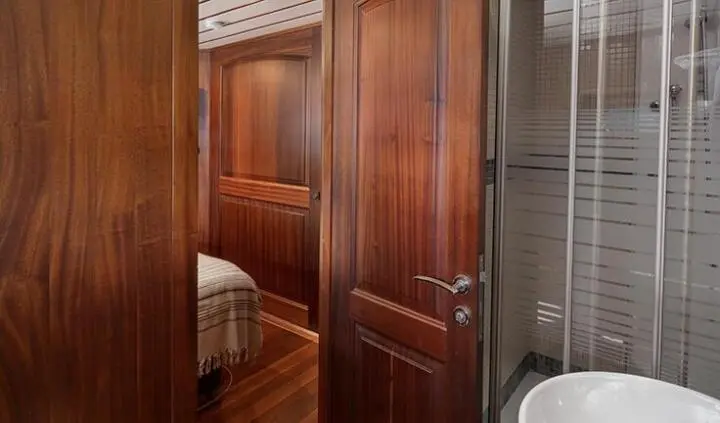 Master cabin with king bed, wood panels, door, and en-suite glimpse