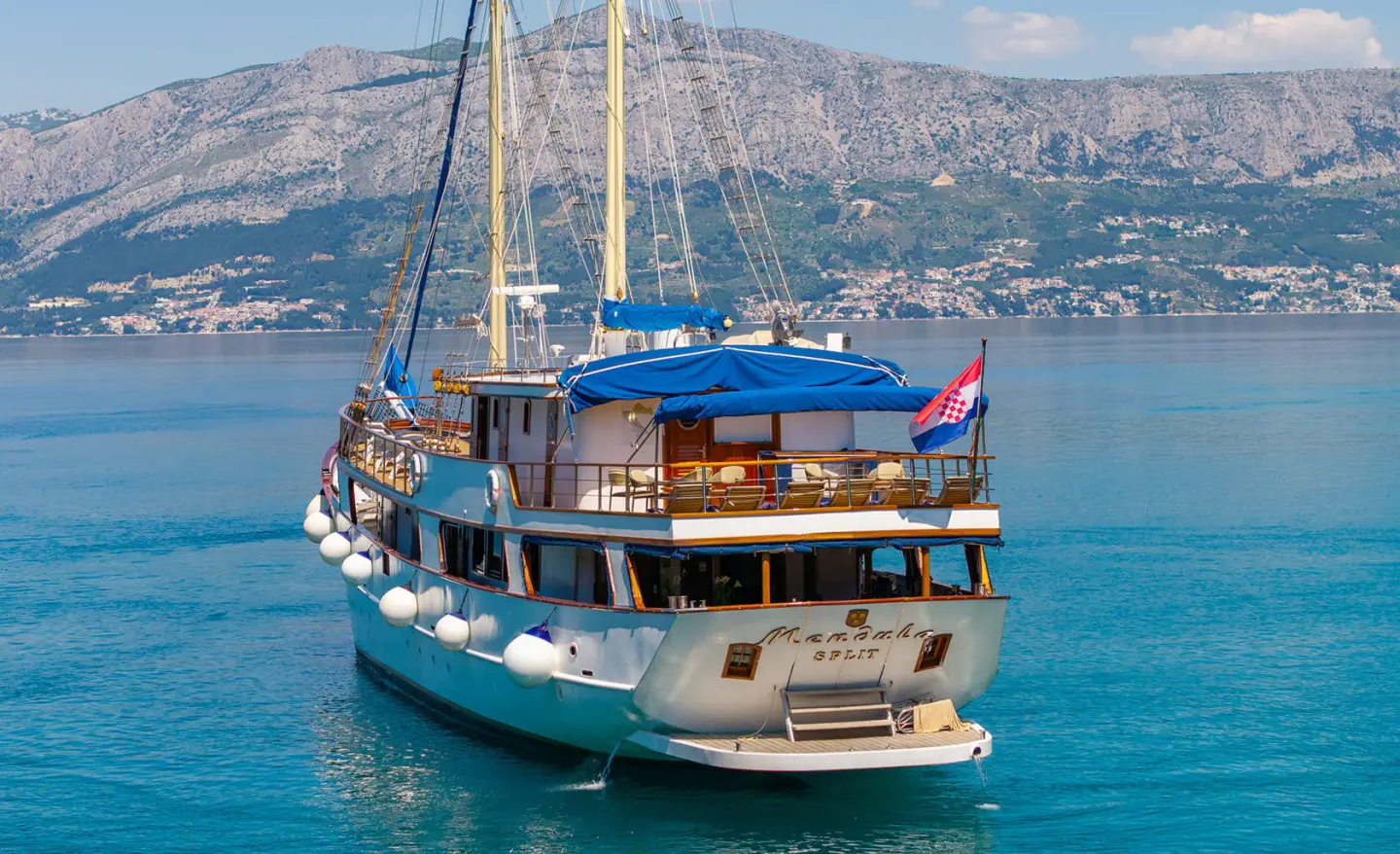 Mendula yacht anchored in blue harbor with sails and warm sunset glow