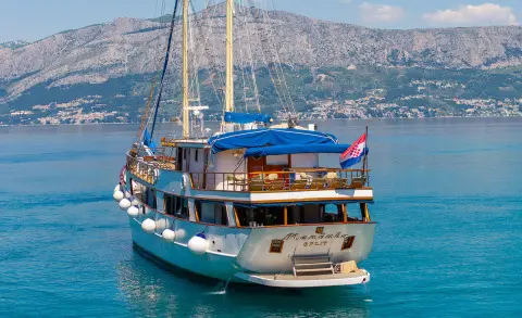 Mendula yacht anchored in blue harbor with sails and warm sunset glow