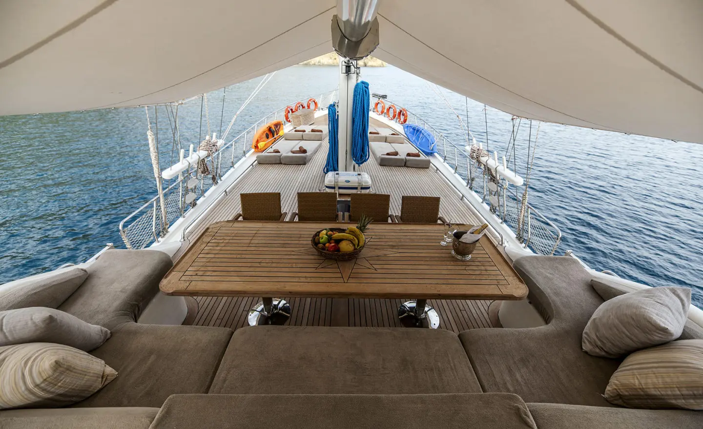 Kayhan 3 yacht deck with shaded seating, wooden table, and ocean view at sunset