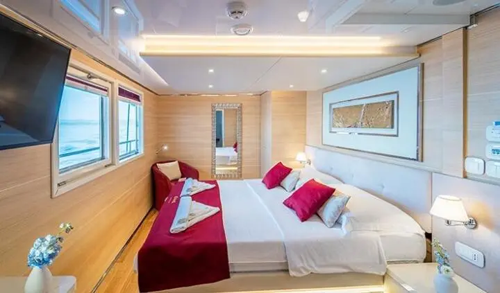 Riva yacht master cabin with two large beds, white linens, red accent pillows