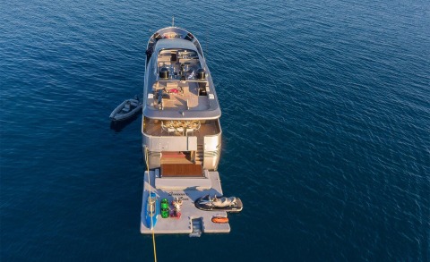 Aerial view of Summer Fun yacht anchored on calm blue sea, with upper deck lounge and watercraft nearby
