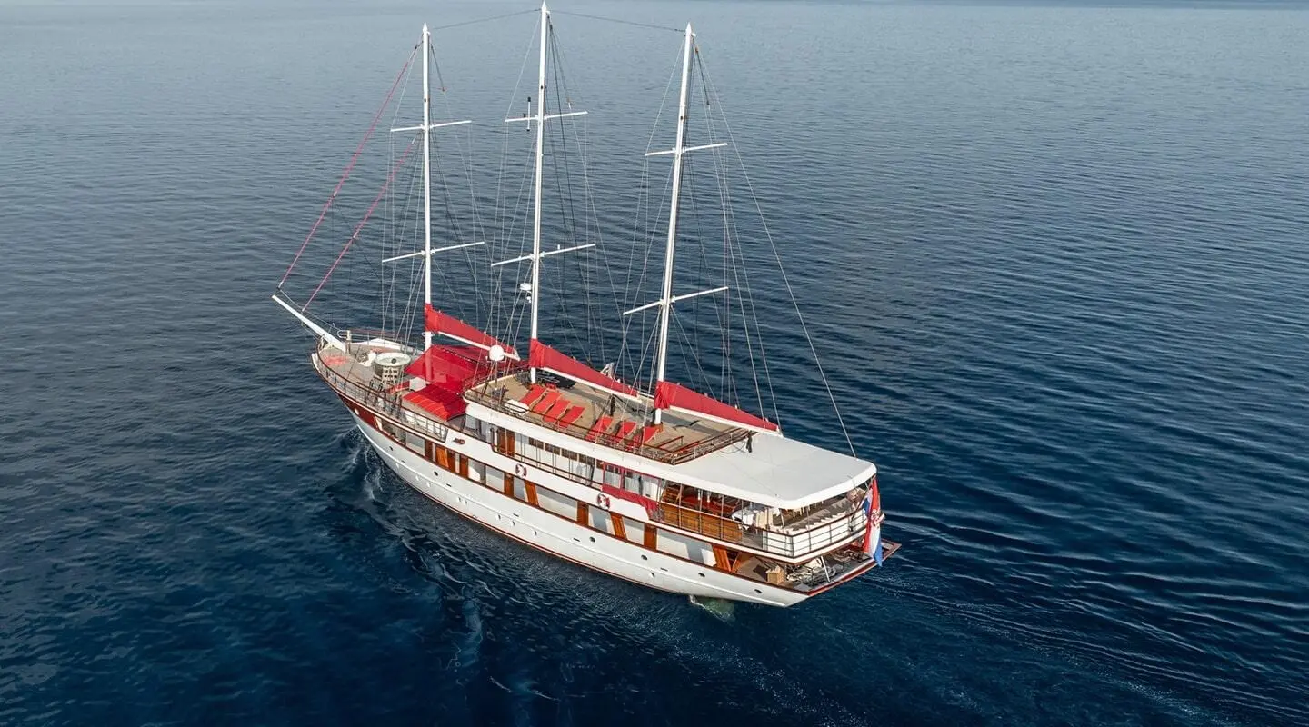 A red and white sailing yacht named Barbara sails calm blue sea