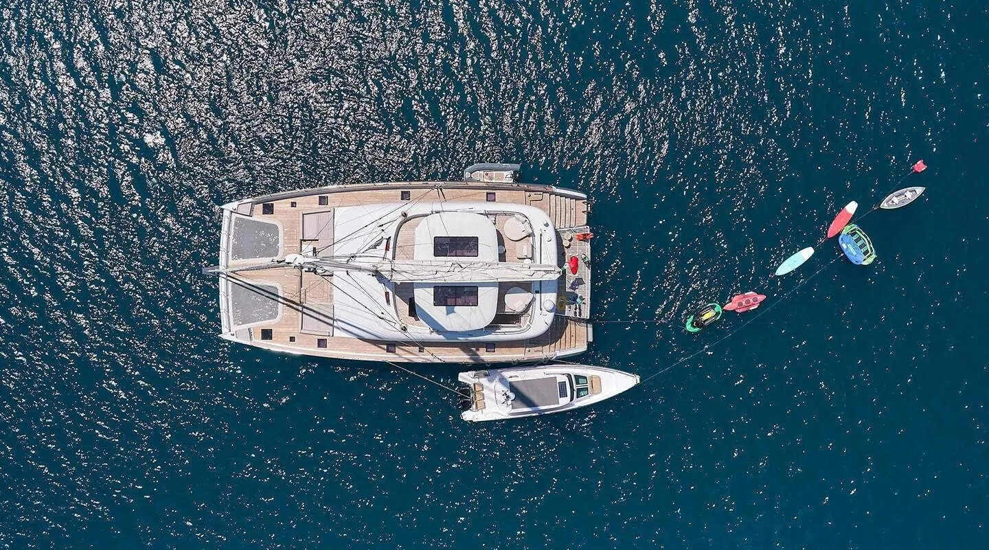 Aerial view of a yacht with a wooden deck and seating areas, moored in blue sea