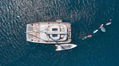 Aerial view of a yacht with a wooden deck and seating areas, moored in blue sea