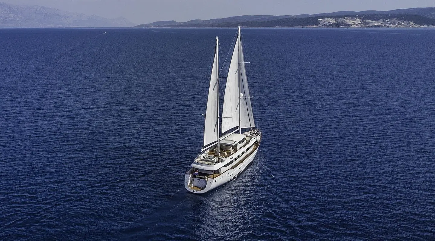 Omnia yacht travels on calm blue sea with white sails catching sunset light