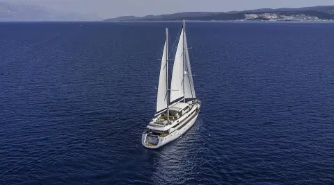 Omnia yacht travels on calm blue sea with white sails catching sunset light