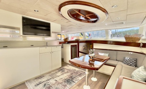 Luxurious gulet interior, wooden table, seating area and cabinets, sunlit with upper deck windows