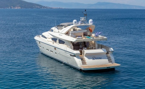 White motor yacht anchored, viewed from the side with deck spaces and stern stairs