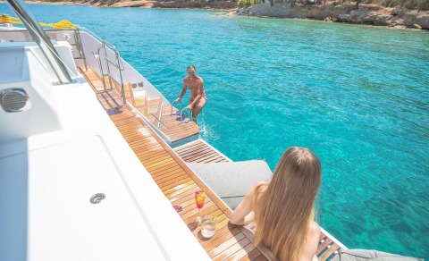 People on the yacht's wooden deck near the water, ladder to the sea visible