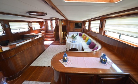 Prenses Bugce interior: elegant mahogany yacht salon with curved white sofa, colorful cushions, dining table, and large windows