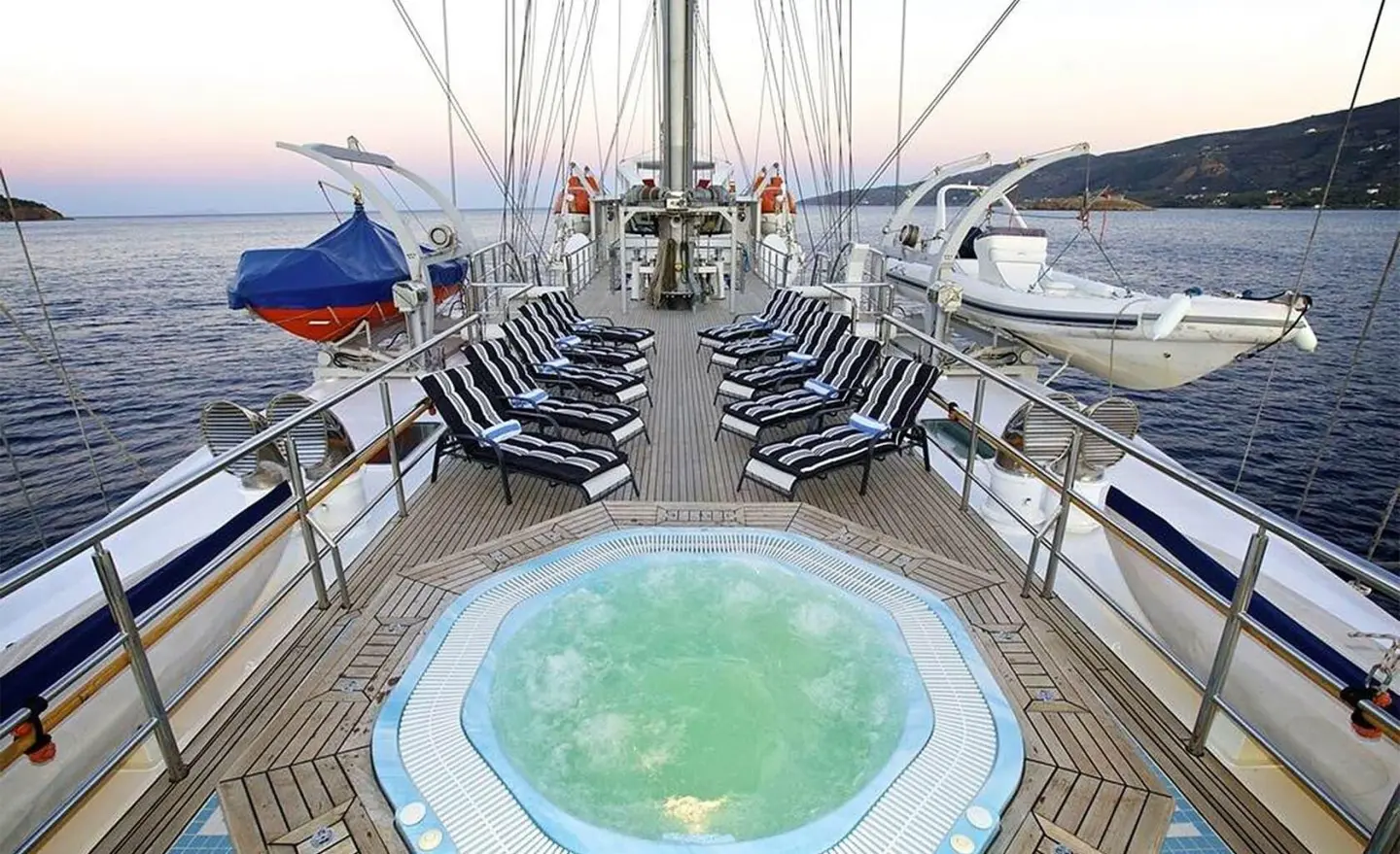 From on-deck view toward a hot tub, chairs line the yachts sides at sunset