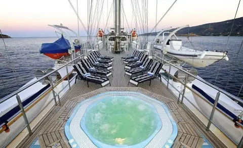 From on-deck view toward a hot tub, chairs line the yachts sides at sunset