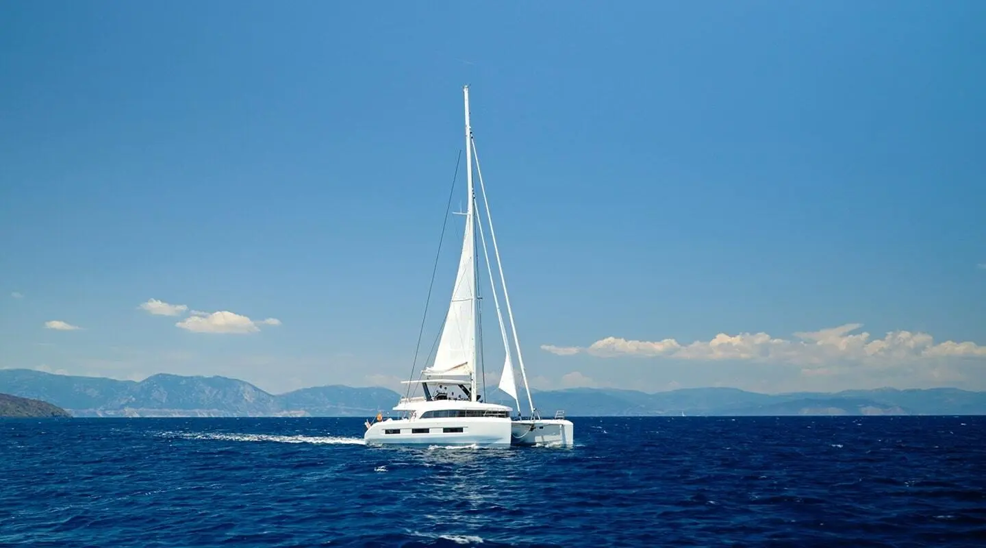 White sailing yacht on open sea with sails up, distant mountains and blue sky