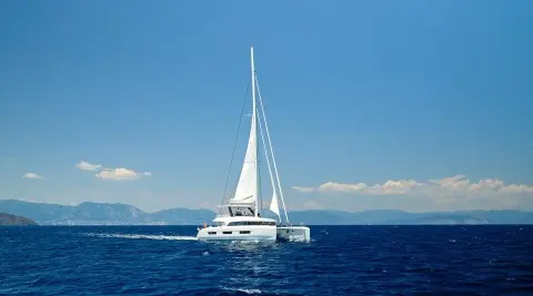 White sailing yacht on open sea with sails up, distant mountains and blue sky