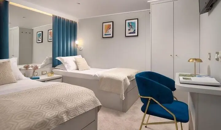 Bellezza yacht cabin with two single beds, blue chair, framed pictures on wall