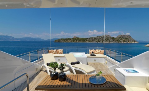 Idylle yacht sun deck with loungers, table and cushions overlooking blue sea